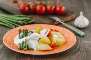 Potatoes and asparagus with tomatoes and tartar sauce on plate ready to eat.