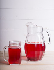 Fresh and healthy red Fruit juice drink  in a glass and jug on the wooden white table background. Side view.