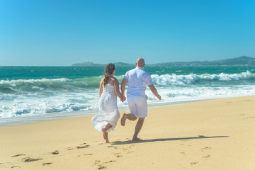 Fototapeta na wymiar Young romantic couple running on the beach holding hands