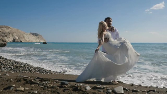 Portrait of the groom turn around himself with bride in arms on the beach