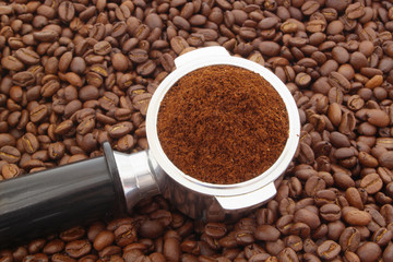 Ground coffee in coffee maker portafilter on coffee beans background, espresso symbol