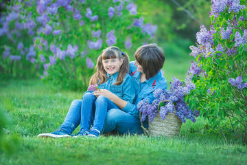 Cute adorable beautifull mother lady mom woman with brunette girl daughter in meadow of lilac purple bush.People in jeans wear.