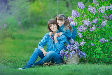 Fototapeta premium Cute adorable beautifull mother lady mom woman with brunette girl daughter in meadow of lilac purple bush.People in jeans wear.
