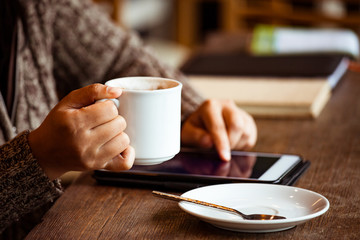 Woman hand holding the cup of coffee and using digital tablet in the cafe in rainy day in vintage color tone