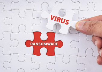 "RANSOMWARE" word on missing puzzle with a hand hold a piece of "VIRUS" word puzzle want to complete it