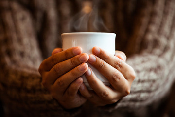 Woman hand holding the cup of coffee or tea in the cafe in rainy day in vintage color tone