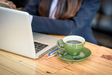 A cup of coffee is on the table beside the laptop computer. By a beautiful young businesswoman is the background.