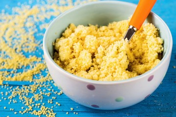 Cooked couscous in bowl on blue background, closeup.
