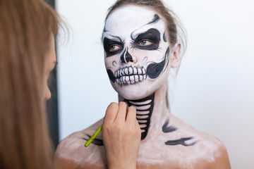Make-up artist make the girl halloween make up on white background. Halloween face art.