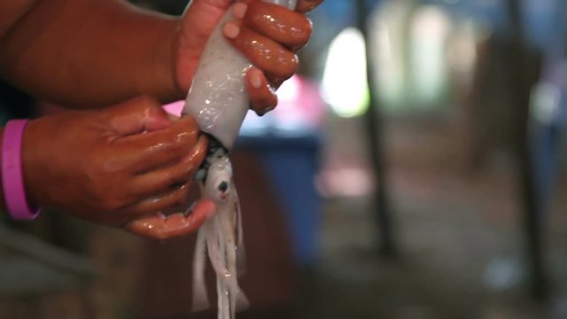 A woman cleans a freshly caught squid for a buyer on the market
