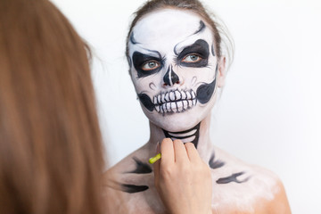 Make-up artist make the girl halloween make up on white background. Halloween face art.