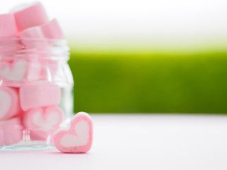 Closeup of sweet marshmallow in the shape of heart on wooden plate and flower at background....