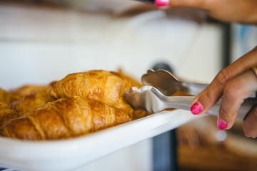 Woman taking croissant with tongs