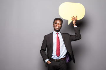Handsome Afro American man in classic suit is holding a speech bubble and thinking, standing against gray