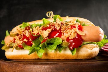 Tasty classic traditional american hot dog with sausages and ketchup on wooden board on dark background.