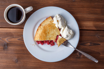 Fresh homemade pie with cherry pulp and ice cream on a plate. A slice of a cherry pie with a ruddy crust on a wooden table. Cherry pie and mug of delicious hot black coffee.