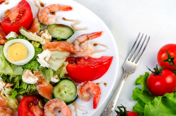 Salad with vegetables and shrimps in a white dish. On a light background.