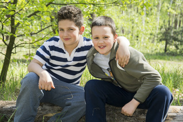 In summer, two friends sit on a long log in the forest.