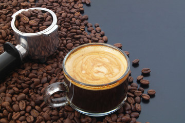 Cup of espresso coffee, coffee machine portafilter and roasted coffee beans on table