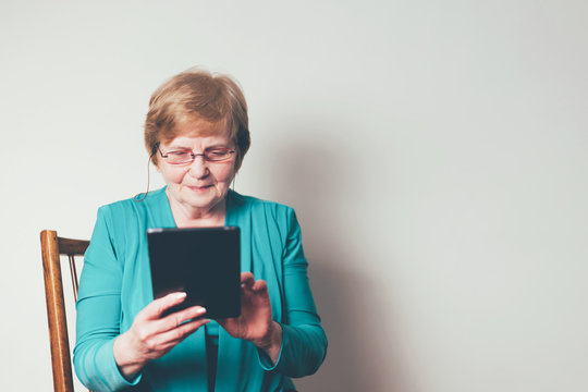 Thoughtful and smiling old woman searching on tablet