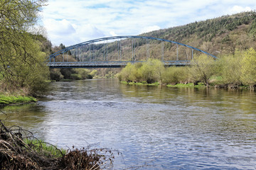 Fototapeta na wymiar Metal bridge arch between scrubby river banks