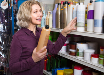 Mature woman selecting shampoo in store.