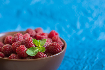 Fresh raspberry in ceramic bowl on the blue background
