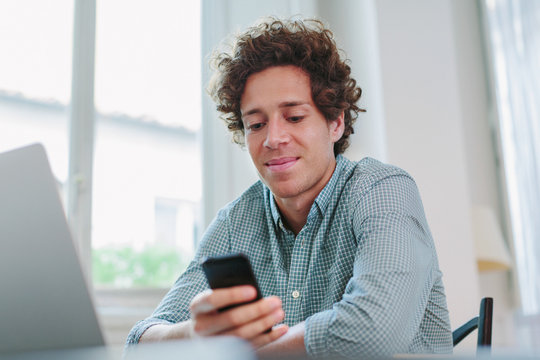 Young free lancer holding mobile phone sitting at desk