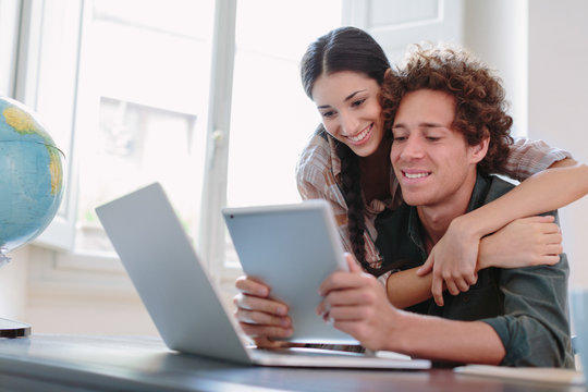 Woman embracing boyfriend working with laptop and tablet happy