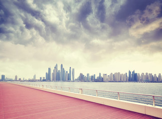 Fototapeta premium Vintage toned picture of rainy clouds over Dubai waterfront skyline seen from a boardwalk, United Arab Emirates.