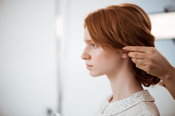 Fototapeta premium Female hairdresser making hairstyle to redhead girl in beauty salon.