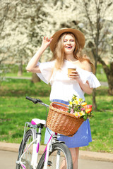 Beautiful smiling girl near bicycle with cup of coffee in park