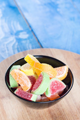 Colorful jelly candies in the bowl above blue background board.