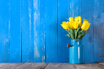 Bouquet of yellow tulips in vase on a blue background