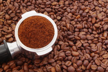 Ground coffee in coffee maker portafilter on coffee beans background, espresso symbol