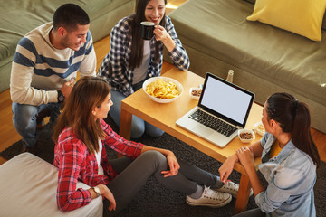 Group of friends sitting together in living room and watching movie on on laptop.Home party.