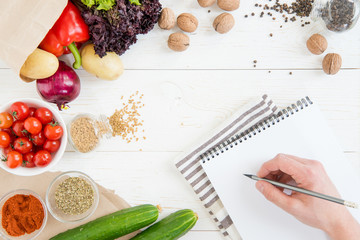 Close-up partial view of person holding pencil and writing recipe in cookbook while cooking