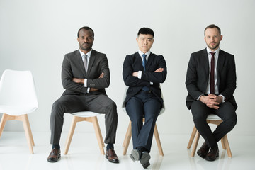 front view of multiethnic businessmen sitting on chairs isolated on white, multicultural business...