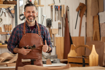 Happy Carpenter/Middle ages handsome carpenter finished creating cabriolet legs and smiles to the camera - obrazy, fototapety, plakaty