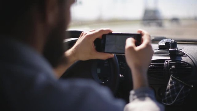 A man with a beard paves the route on a smartphone while sitting in the car