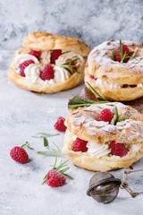 Homemade choux pastry cake Paris Brest with raspberries, almond, sugar powder and rosemary, served over gray blue texture background. Close up. French dessert