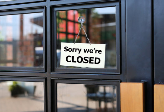 Sorry we're Closed sign board hanging on door of cafe.