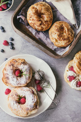 Filling and empty homemade choux pastry cake Paris Brest with raspberries, almond, sugar powder, rosemary on plate and oven tray with berries over gray texture background. French dessert. Flat lay