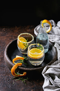 Tonic water cocktail with rosemary and orange. Two glasses and bottle with zest sugar and bubbles in terracotta tray over black texture background. Refreshing beverage alco non alcohol
