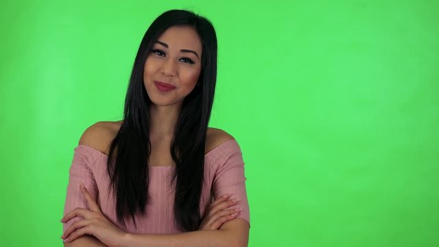 young attractive asian woman smiles to camera with folded arms - green screen