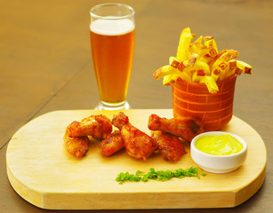 Delicious grilled chicken wings with french fries, ketchup, mustard and a glass of beer on wooden board