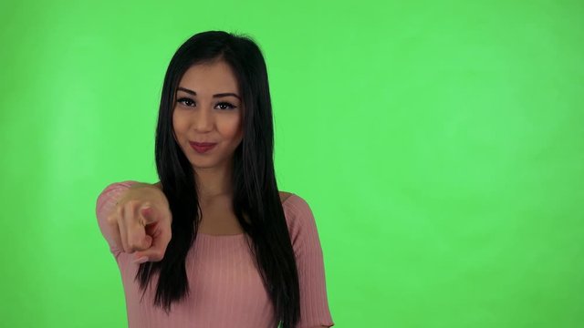 young attractive asian woman points to camera - green screen studio