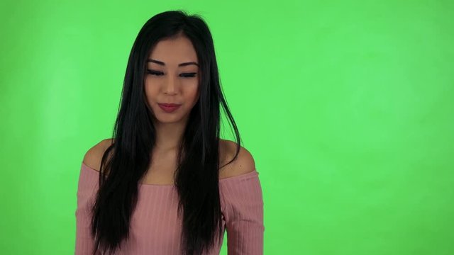 young attractive asian woman points to watch - green screen studio