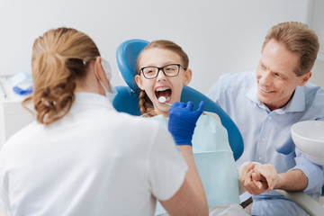 Adorable positive girl visiting dentist with her dad