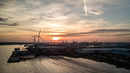 Dusk at the Port of Tilbury, Essex, UK. Sunset view of the low tide of the River Thames and wind turbines turning in the background.